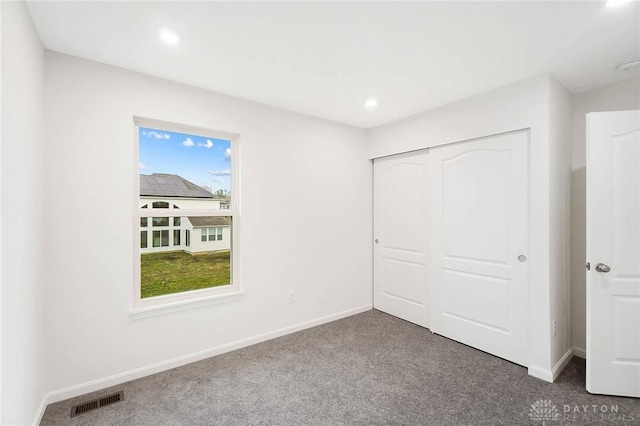 unfurnished bedroom featuring multiple windows, dark carpet, and a closet