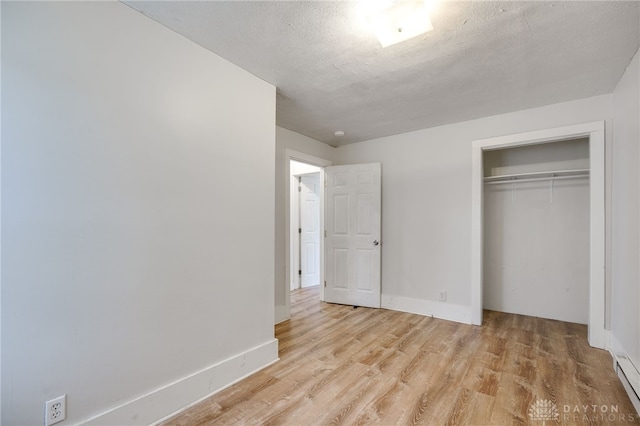 unfurnished bedroom with a baseboard radiator, light hardwood / wood-style floors, a closet, and a textured ceiling