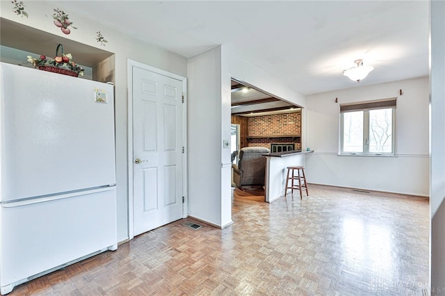 kitchen featuring a brick fireplace, a breakfast bar, light parquet flooring, and white fridge