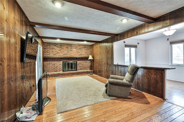 unfurnished living room with light hardwood / wood-style flooring, beam ceiling, a fireplace, and wood walls