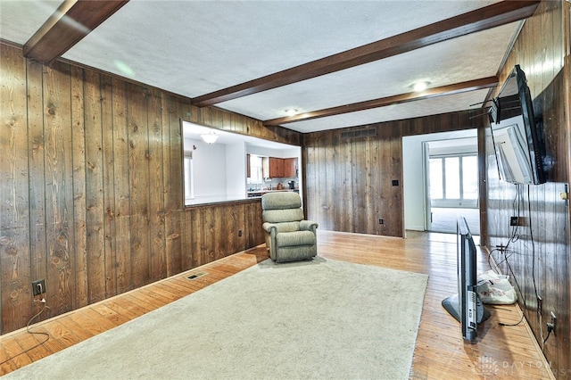 sitting room featuring light hardwood / wood-style flooring, beam ceiling, wooden walls, and a textured ceiling