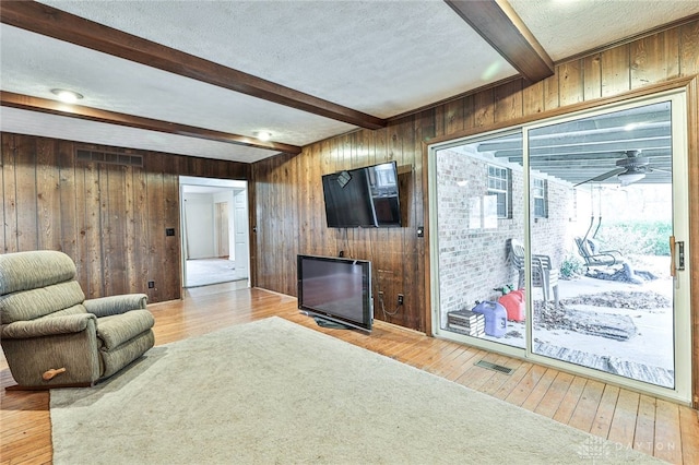 living room featuring wooden walls, a textured ceiling, beam ceiling, and light hardwood / wood-style flooring