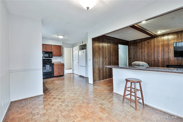 kitchen with a breakfast bar area, wood walls, black appliances, kitchen peninsula, and light parquet floors