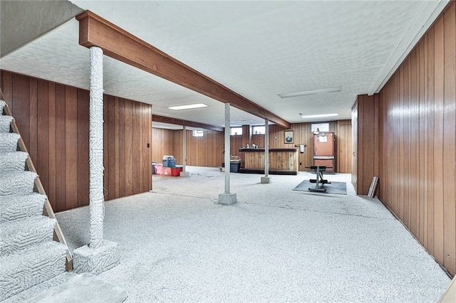 basement featuring carpet flooring, a textured ceiling, and wood walls