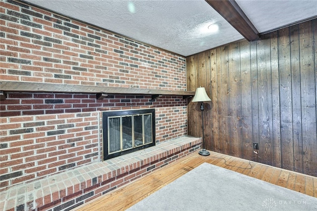 living room featuring hardwood / wood-style flooring, wooden walls, a textured ceiling, a brick fireplace, and beamed ceiling