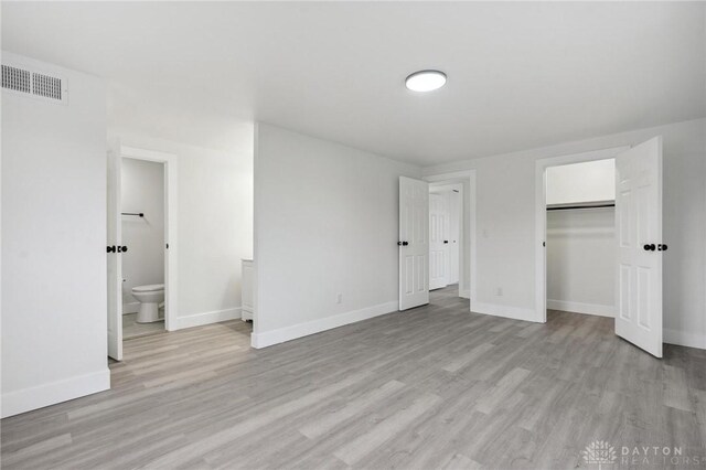 unfurnished bedroom featuring ensuite bath, a closet, and light wood-type flooring