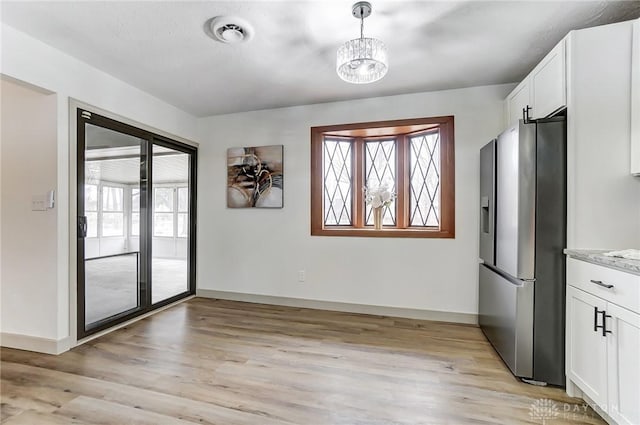 interior space featuring white cabinetry, light stone counters, decorative light fixtures, light hardwood / wood-style flooring, and stainless steel fridge