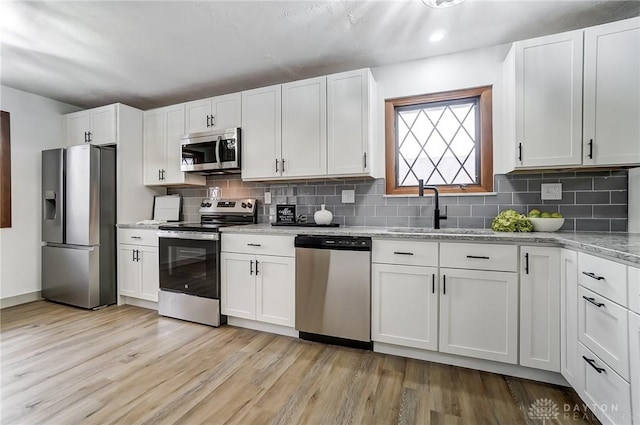 kitchen featuring white cabinetry, tasteful backsplash, light stone counters, light hardwood / wood-style flooring, and stainless steel appliances