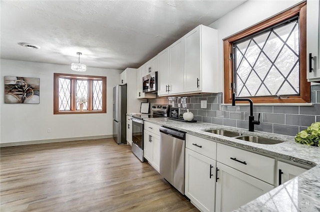 kitchen with stainless steel appliances, light stone countertops, sink, and white cabinets