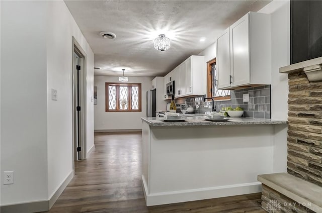 kitchen with white cabinetry, stainless steel appliances, light stone counters, decorative backsplash, and kitchen peninsula