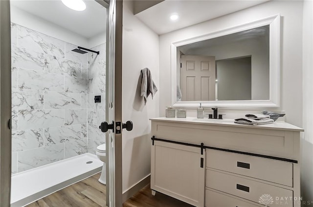 bathroom with vanity, toilet, wood-type flooring, and a tile shower