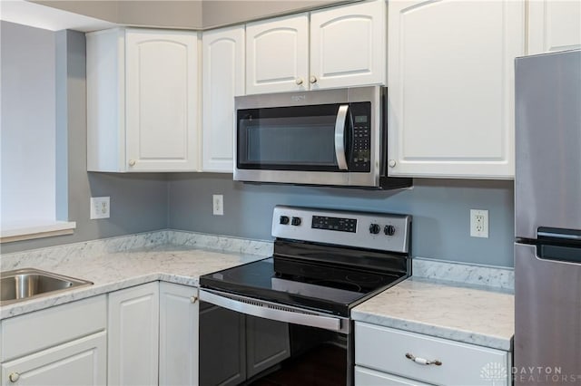 kitchen with stainless steel appliances, light stone countertops, and white cabinets