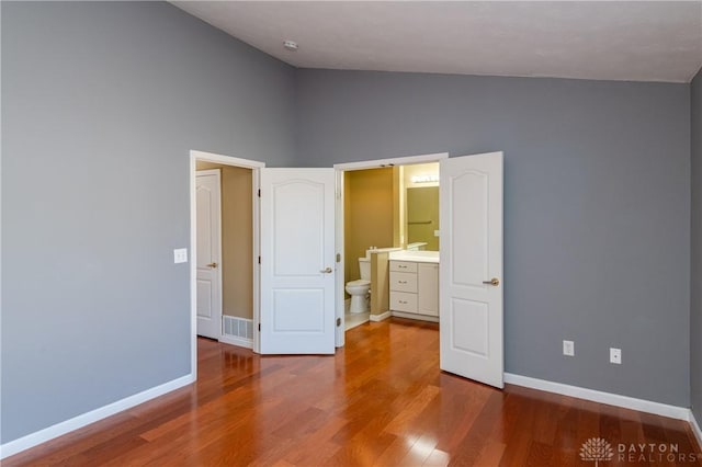 unfurnished bedroom with connected bathroom, vaulted ceiling, and wood-type flooring