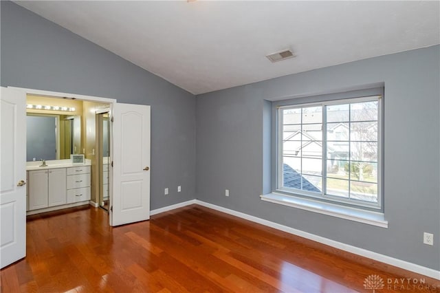 unfurnished bedroom with hardwood / wood-style flooring, lofted ceiling, sink, and ensuite bath