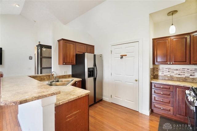 kitchen featuring sink, decorative light fixtures, vaulted ceiling, kitchen peninsula, and stainless steel appliances