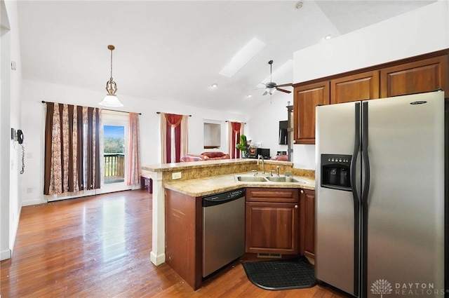 kitchen featuring appliances with stainless steel finishes, vaulted ceiling with skylight, decorative light fixtures, sink, and dark wood-type flooring