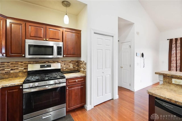 kitchen featuring vaulted ceiling, appliances with stainless steel finishes, pendant lighting, light hardwood / wood-style floors, and backsplash