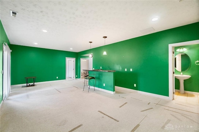 interior space with light colored carpet, wet bar, and a textured ceiling