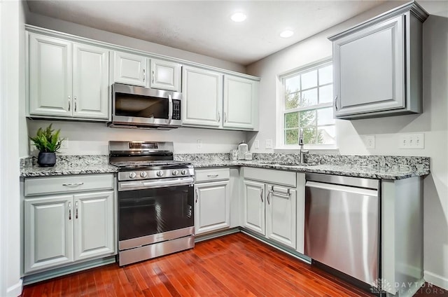 kitchen with sink, light stone countertops, dark hardwood / wood-style floors, and appliances with stainless steel finishes