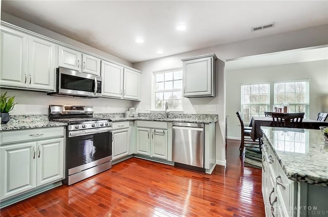 kitchen featuring appliances with stainless steel finishes, sink, light stone counters, and dark hardwood / wood-style flooring