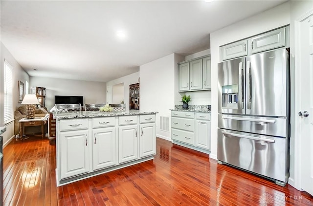 kitchen with stainless steel fridge, light stone countertops, dark hardwood / wood-style floors, and a center island