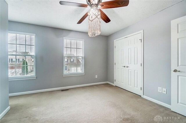 unfurnished bedroom with light colored carpet, a closet, and ceiling fan