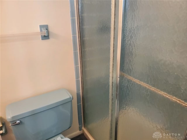 bathroom featuring a shower with door and toilet