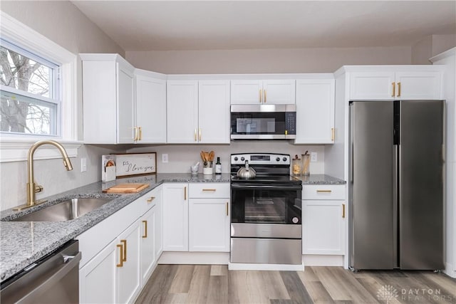 kitchen with sink, white cabinets, stainless steel appliances, light stone countertops, and light wood-type flooring