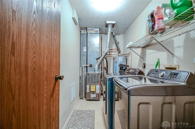 laundry room featuring water heater, washing machine and dryer, and a textured ceiling