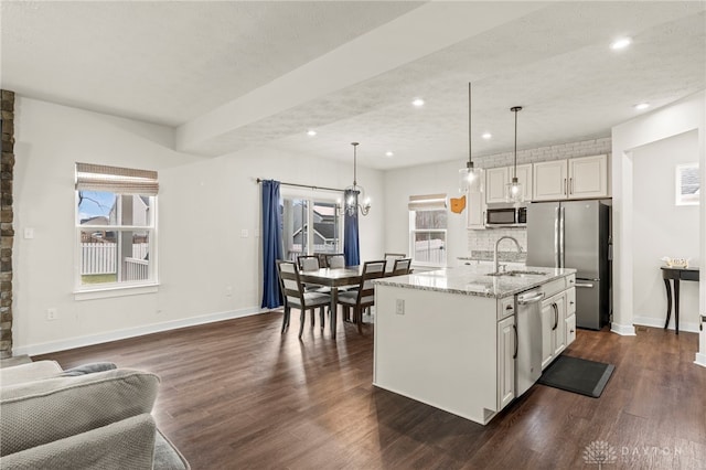 kitchen with appliances with stainless steel finishes, decorative light fixtures, sink, light stone counters, and a center island with sink