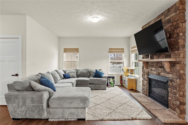 living room featuring hardwood / wood-style flooring, a stone fireplace, and a textured ceiling