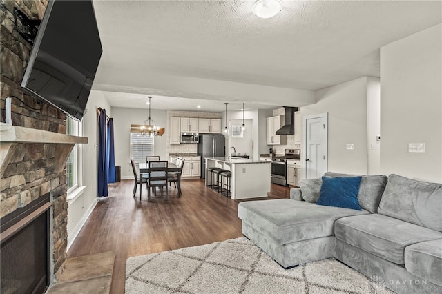 living room featuring sink, dark hardwood / wood-style floors, a notable chandelier, a fireplace, and a textured ceiling