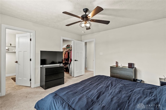 bedroom with ceiling fan, light colored carpet, a textured ceiling, and a walk in closet