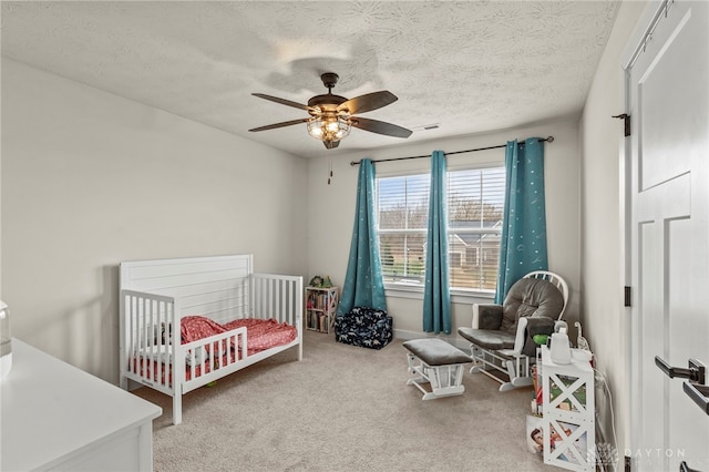 bedroom featuring a nursery area, ceiling fan, carpet floors, and a textured ceiling