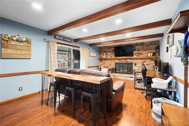 living room featuring beamed ceiling, a brick fireplace, and light wood-type flooring