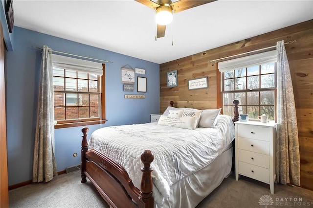 bedroom with ceiling fan, dark carpet, multiple windows, and wood walls