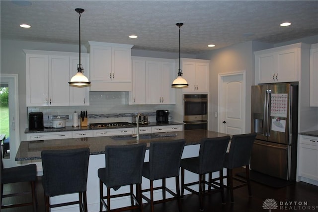 kitchen featuring white cabinetry, appliances with stainless steel finishes, decorative light fixtures, and a center island with sink