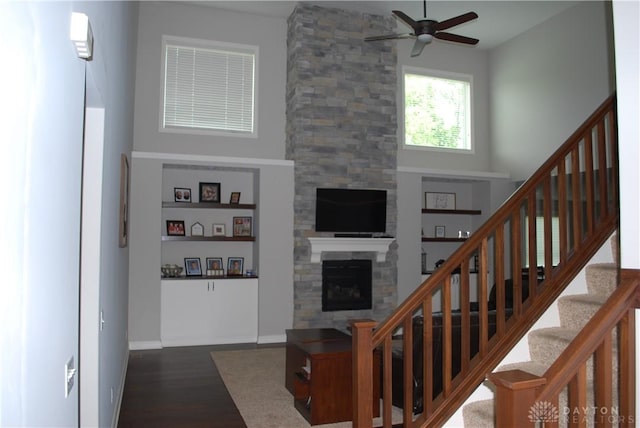 stairway featuring a high ceiling, wood-type flooring, a stone fireplace, and ceiling fan