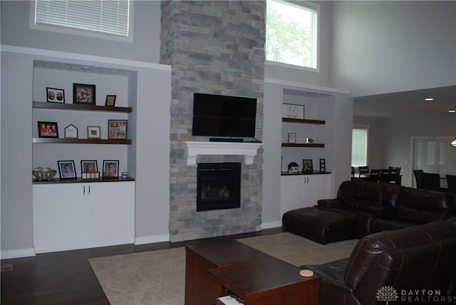 living room featuring built in shelves, a stone fireplace, dark wood-type flooring, and a high ceiling