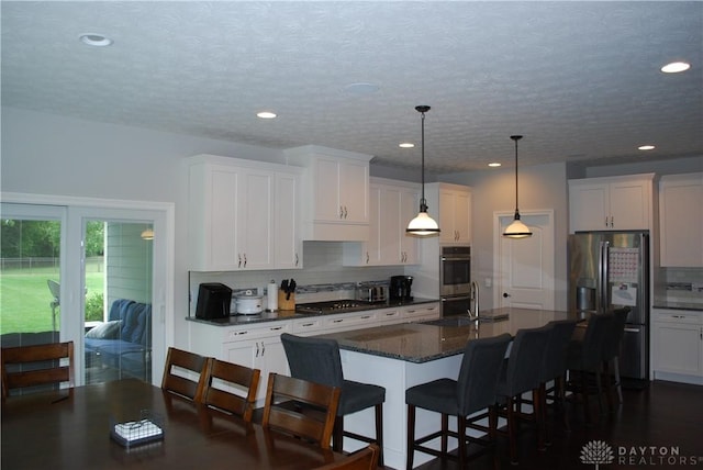 kitchen featuring white cabinetry, hanging light fixtures, stainless steel appliances, and an island with sink