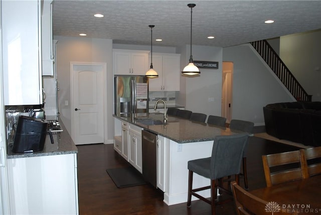 kitchen featuring white cabinetry, hanging light fixtures, dark stone countertops, a center island with sink, and appliances with stainless steel finishes