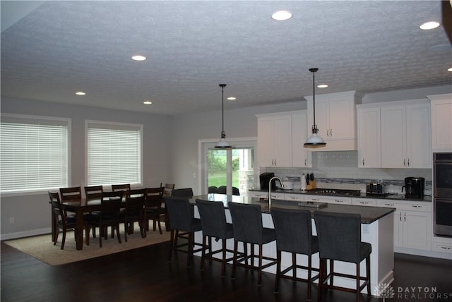 kitchen with hanging light fixtures, a center island with sink, and white cabinets