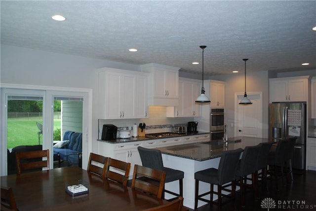 kitchen with a kitchen island with sink, pendant lighting, white cabinetry, and appliances with stainless steel finishes