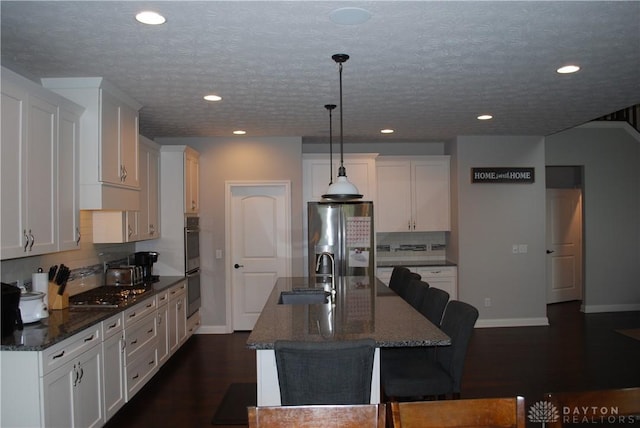 kitchen with sink, appliances with stainless steel finishes, hanging light fixtures, white cabinets, and a center island with sink