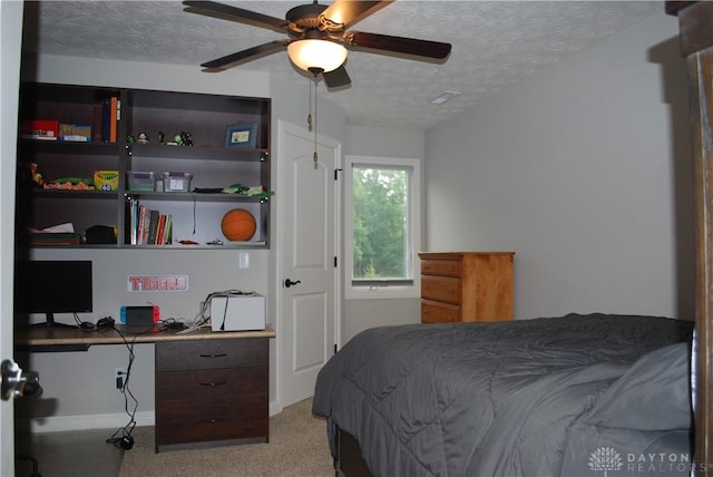 carpeted bedroom featuring ceiling fan, built in desk, and a textured ceiling