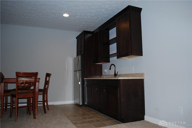 kitchen with tile patterned flooring, sink, stainless steel refrigerator, and a textured ceiling