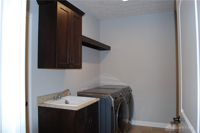 clothes washing area with cabinets, sink, washer and dryer, and a textured ceiling