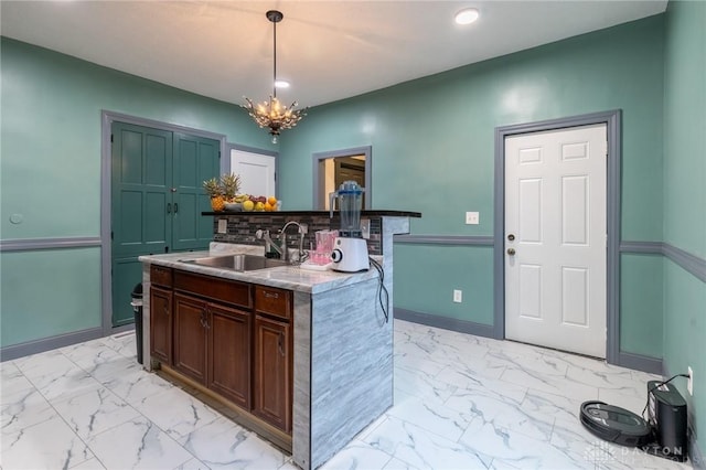 kitchen featuring decorative light fixtures, an island with sink, sink, a notable chandelier, and dark brown cabinets