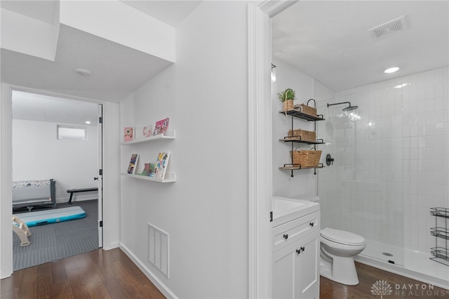 bathroom with a tile shower, vanity, hardwood / wood-style flooring, and toilet