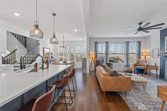 living room with dark wood-type flooring, ceiling fan with notable chandelier, and sink